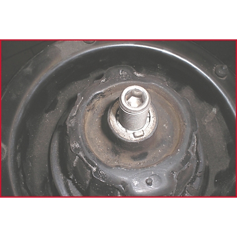 Nahaufnahme einer Fahrzeugaufhängung. Ein Schraubbolzen steht im Mittelpunkt, umgeben von Metallteilen, die auf Abnutzung hindeuten.